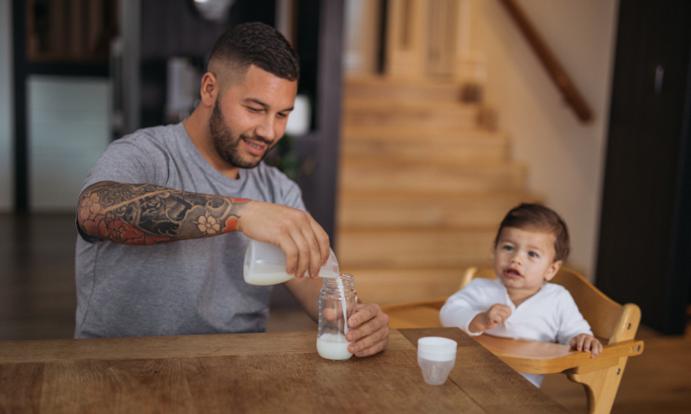 Tattooed Dad is pouring breast milk from Pumpd silicone breast pump into baby bottle to feed to his son