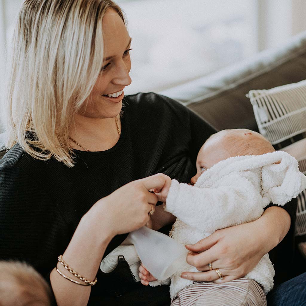 Mum holding newborn baby while using the Pumpd breast pump to collect let down