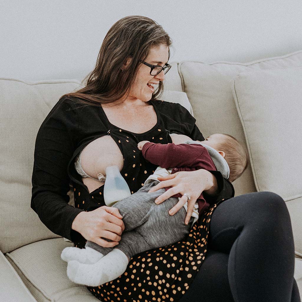 Young mum breastfeeding baby while using Pumpd Breast Pump to collect breastmilk