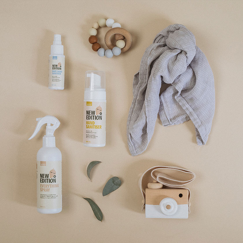 Flat lay image of the sanitiser range accompanies by a baby teething toy, muslin cloth, toy camera and olive leaves