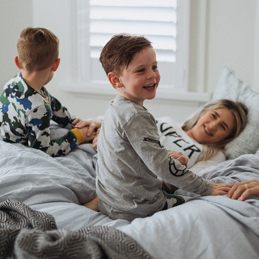 mum and dad lying in bed in the morning with her two sons smiling and laughing with them in their pajamas
