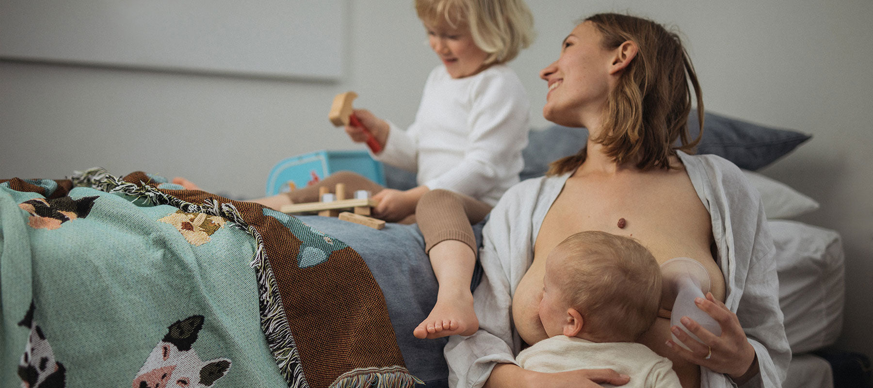 Young mum breastfeeding newborn while using the Pumpd manual breast pump to collect breast milk on her other boob