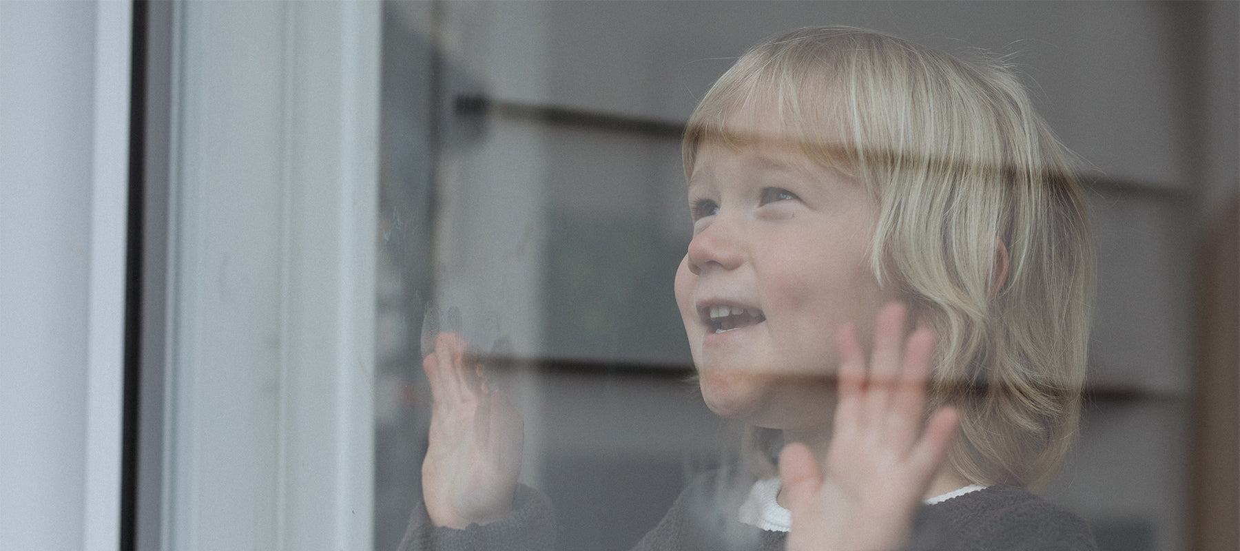 photo of young boy looking through the window with his hands on the glass smiling