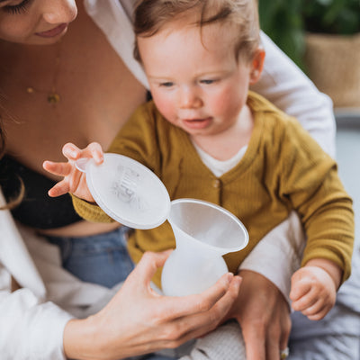 after pumping and collecting breast milk with the Pumpd breast pump mum is showing her baby and he is playing with the lid