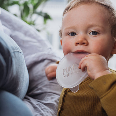 teething toddler is looking at the camera and using the soft Pumpd breast pump lid to chew on