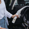 Mum in blue jeans and white top using the New Edition Everything Spray surface sanitiser to clean baby pram capsule while it is in the car